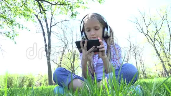 儿童在公园玩平板电脑女孩带耳机在夏季户外4K视频的预览图