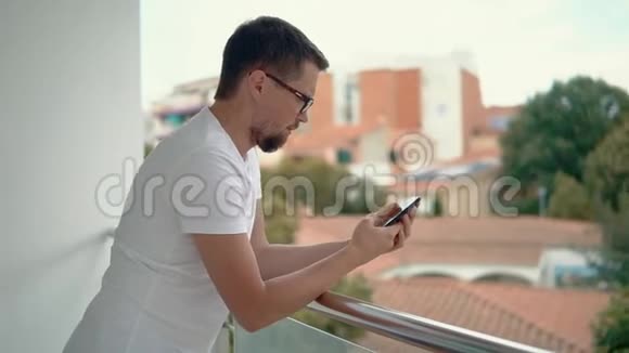 成年胡须男靠在阳台的扶手上通过电话看信息视频的预览图