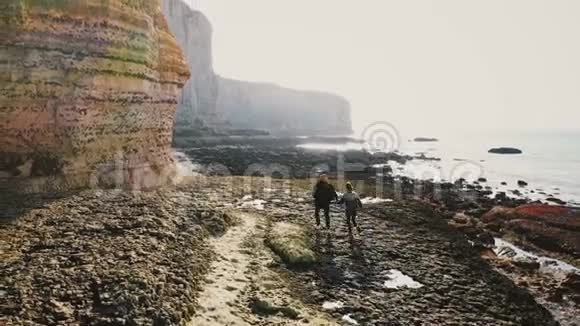 在诺曼底的史诗般的岩石下一对快乐的游客沿着不可思议的低潮珊瑚和卵石海岸奔跑视频的预览图