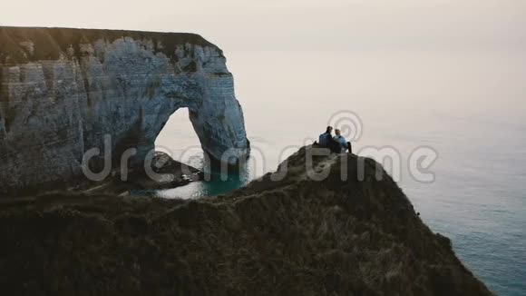 美丽的无人机在欢乐的朋友的视野中坐在一起观看诺曼底海岸悬崖上的日落海视频的预览图