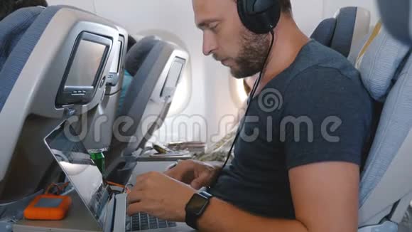 年轻的快乐专注自由职业商人与智能手表使用笔记本电脑在移动办公室工作期间飞机飞行视频的预览图
