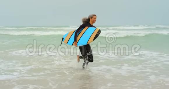 活跃的非裔美国女性冲浪者在海滩上朝大海奔跑的侧面景色视频的预览图
