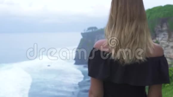 幸福的女人在海边欣赏山崖和海浪景观在山崖边微笑的女人视频的预览图