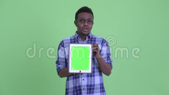 年轻快乐的非洲时髦男人一边说一边展示数字平板电脑视频的预览图