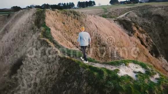 后景青年游客男子走在危险的狭窄陡峭的小径上在日落悬崖上女人等着他视频的预览图