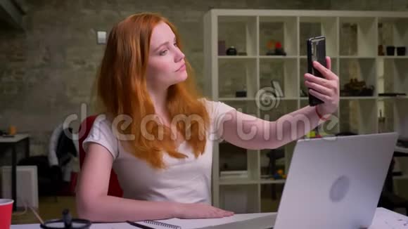 可爱的红发白种人女性正在自拍集中脸靠近她的笔记本电脑在桌面轻办公室视频的预览图