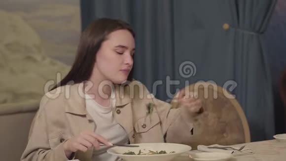 一位留着长发的年轻女士坐在餐桌前吃着蔬菜和蔬菜的面条视频的预览图