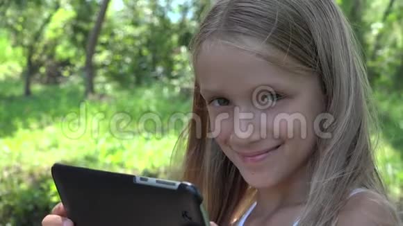 大自然中的童玩平板电脑荡秋千中的微笑女孩玩电脑游戏4K视频的预览图