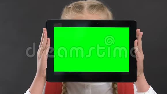 女生手持平板电脑面前有绿色屏幕在线上课视频的预览图