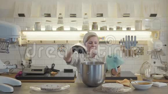穿着制服戴着黑手套的妇女站在现代厨房里周围摆着许多厨房用具并涂上白色的奶油视频的预览图