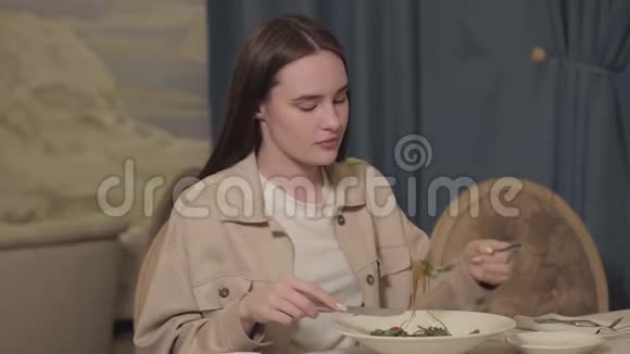 留着长发的漂亮女人坐在餐厅的桌子旁吃着青菜和蔬菜的面条孤独的女人视频的预览图