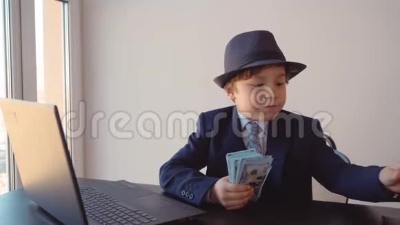 小男孩看起来像一个戴帽子和西装的商人用放大镜检查美元视频的预览图