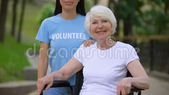 坐轮椅的成熟的快乐女人和寻找相机的年轻志愿者视频的预览图