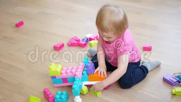 可爱的小女孩在地板上玩五颜六色的建筑塑料块视频的预览图