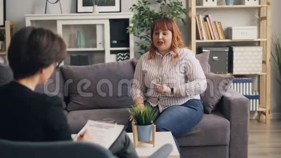 肥胖的女孩与治疗师分享问题坐在沙发上说话和打手势视频的预览图
