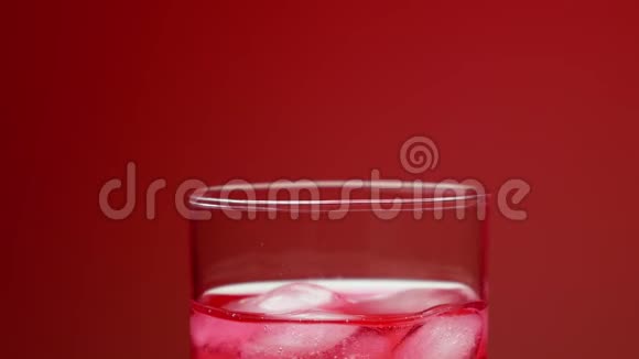 冰块落在杯子里用红色苏打水溅起水花和气泡鸡尾酒吸管搅拌慢动作视频的预览图