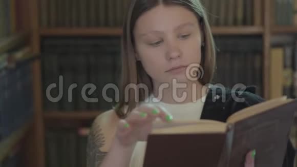 图书馆里有一本书肩上有纹身的可爱女孩的肖像有魅力的年轻女孩视频的预览图