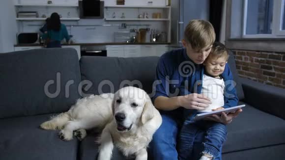 爸爸和蹒跚学步的孩子在沙发上和狗狗在一起视频的预览图