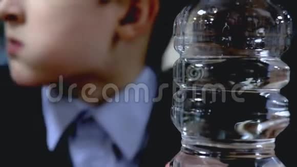 清澈透明的塑料瓶水靠近一个模糊的学童坐在桌子旁嚼着背景视频的预览图