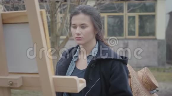 肖像熟练的成功艺术家在后院的画架上作画美丽热情的女孩视频的预览图