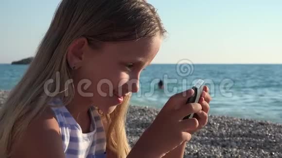 4K女孩在海滩上玩平板电脑日落景观儿童使用智能手机海岸线视频的预览图