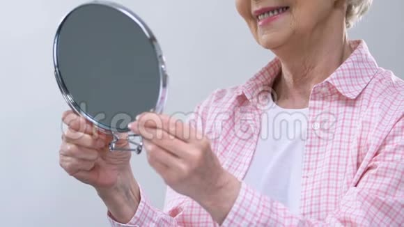 微笑的老年妇女照镜子享受外表美容护理视频的预览图