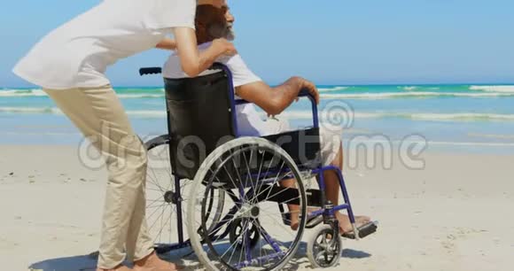 海滩上活跃的非洲裔美国老年妇女拥抱残疾老人的侧视图4k视频的预览图