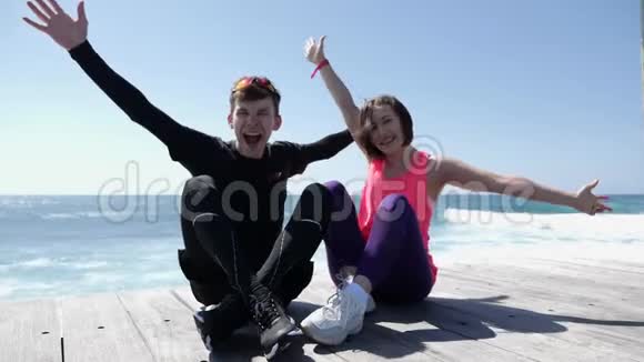 年轻迷人的幸福夫妇举起双手在空中微笑和欢呼坐在海滩上视频的预览图