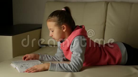 穿着灰色粉色运动衫的可爱女孩子躺在房间的沙发上看书视频的预览图
