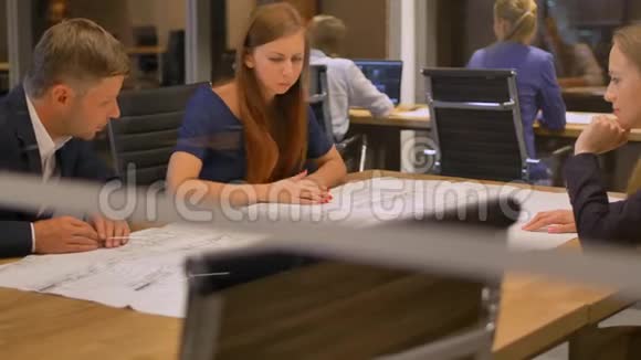 在现代办公室里三个工作人员在桌子旁看着图纸说话视频的预览图