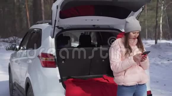 阳光明媚的冬日女孩坐在车里为相机摆出甜美的姿势视频的预览图