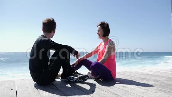 年轻漂亮的女人坐在沙滩上亲吻适合活泼的男人的嘴唇慢动作视频的预览图