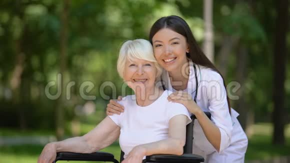 微笑的女护士拥抱残疾的老年妇女看着镜头视频的预览图