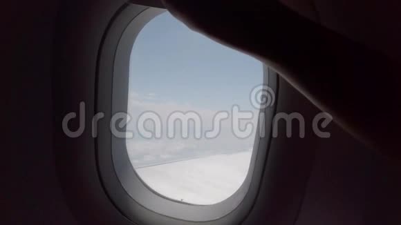 女人的手在关上飞机的窗户从飞机窗户看到的云和天空视频的预览图