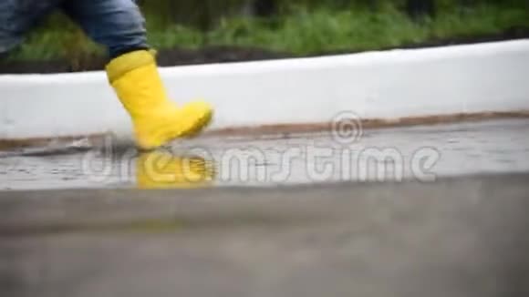 雨后一个穿黄色靴子的孩子穿过水坑视频的预览图