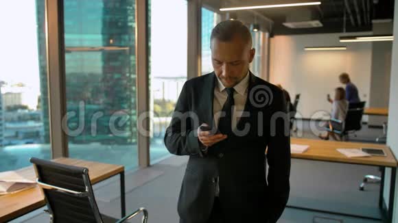 一位有魅力的商人站在窗边写短信的画像视频的预览图