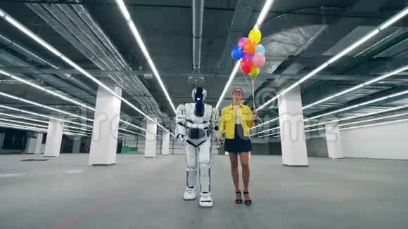 一位带着气球的女士正和一个机器人沿着大厅走视频的预览图