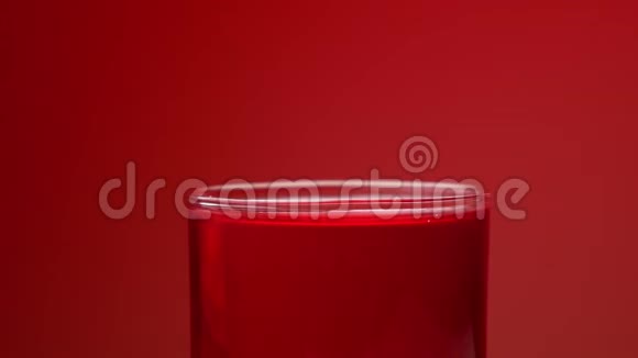 水滴落在玻璃杯里用红色的苏打水起水花和气泡红色背景和慢动作视频的预览图