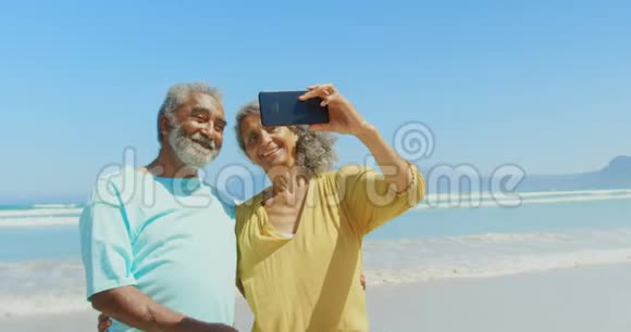 活跃的非裔美国人夫妇在海滩上用手机自拍的正面景色视频的预览图