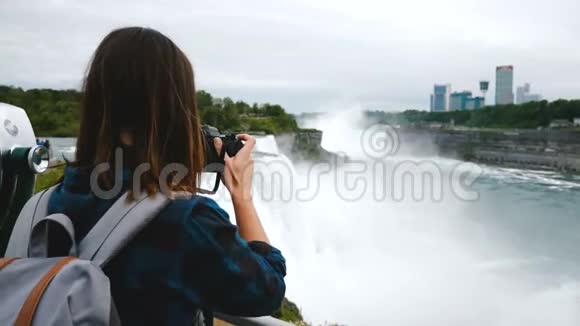 带着背包和相机拍摄史诗尼亚加拉瀑布景慢动作的兴奋旅游妇女的后景视频的预览图