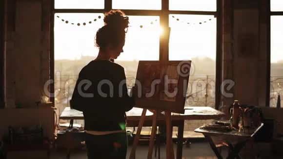 在她20的完全集中老练的女艺术家正在画架上画一个艺术工作室视频的预览图