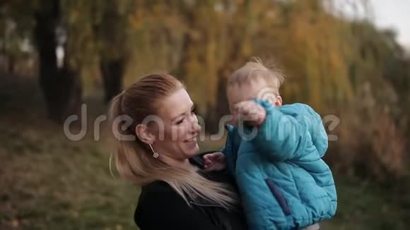 秋天公园里快乐的年轻妈妈拥抱并把小儿子扔在这里的特写镜头视频的预览图