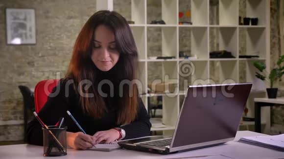 年轻的黑发女商人的肖像在办公室的笔记本上认真地做笔记视频的预览图