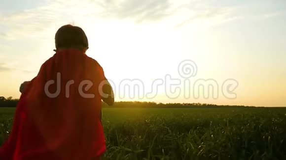 一个穿着超级英雄服装的快乐孩子在夕阳下穿过一片绿色的草坪视频的预览图