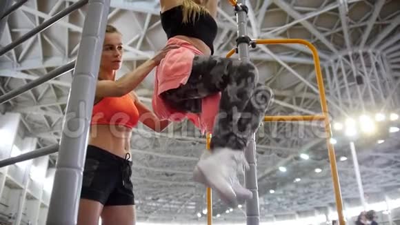 年轻女子在运动场的横杆上拉起在教练的帮助下她的下半身视频的预览图