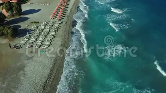 飞越一个带波浪和海浪的卵石海滩希腊罗德斯岛酒店和雨伞的海岸线景色视频的预览图
