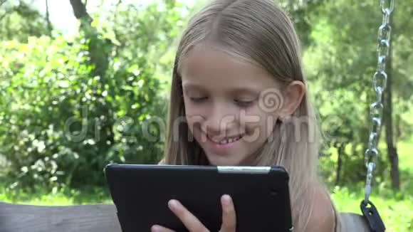 孩子玩平板电脑摇摆女孩在户外使用电脑孩子在花园里视频的预览图