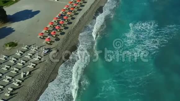 飞越一个带波浪和海浪的卵石海滩希腊罗德斯岛酒店和雨伞的海岸线景色视频的预览图