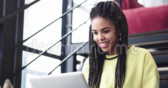 特写非常漂亮的非洲年轻女士在电脑上工作在商务中心她坐在楼梯上还有一个视频的预览图