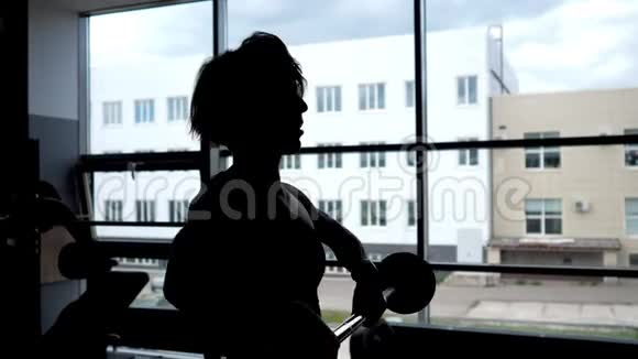 一个女人在窗户上举杠铃做肩部肌肉的剪影视频的预览图